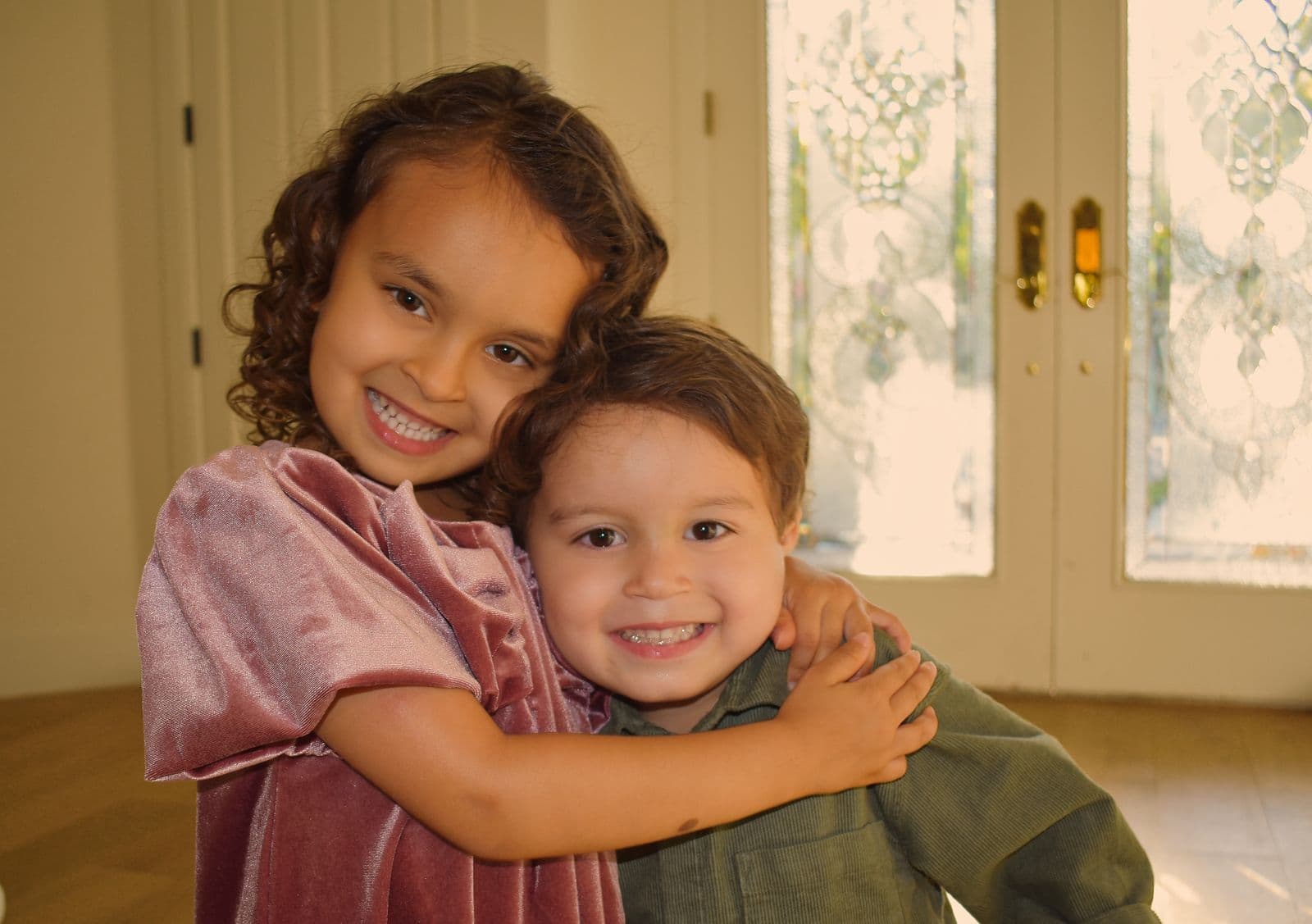 A brother and sister hugging in soft window light during an at-home session in Las Vegas, NV