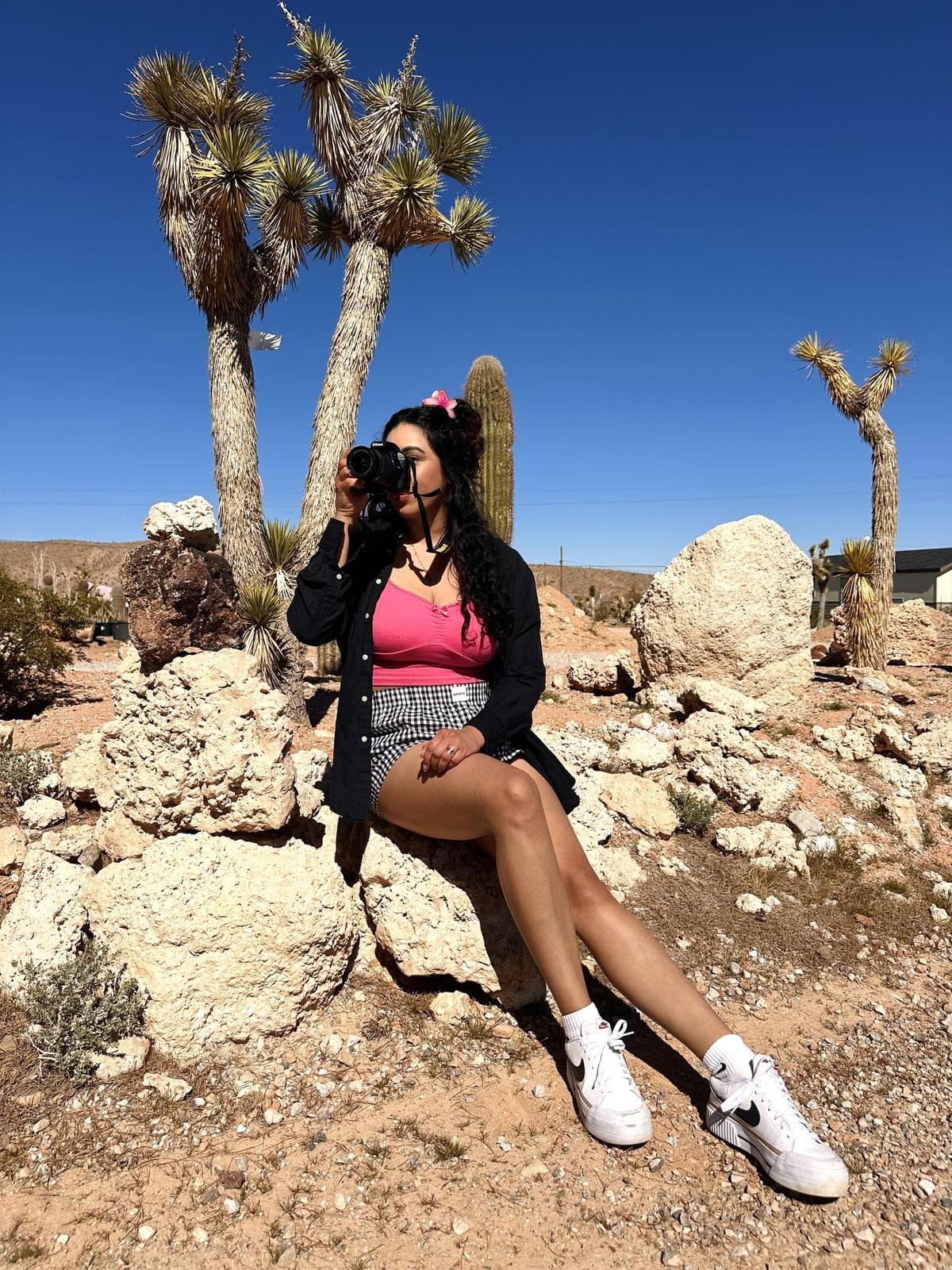 Las Vegas photographer Melyssa Silva shooting on location in the desert, seated on a rock among Joshua trees under a clear blue sky