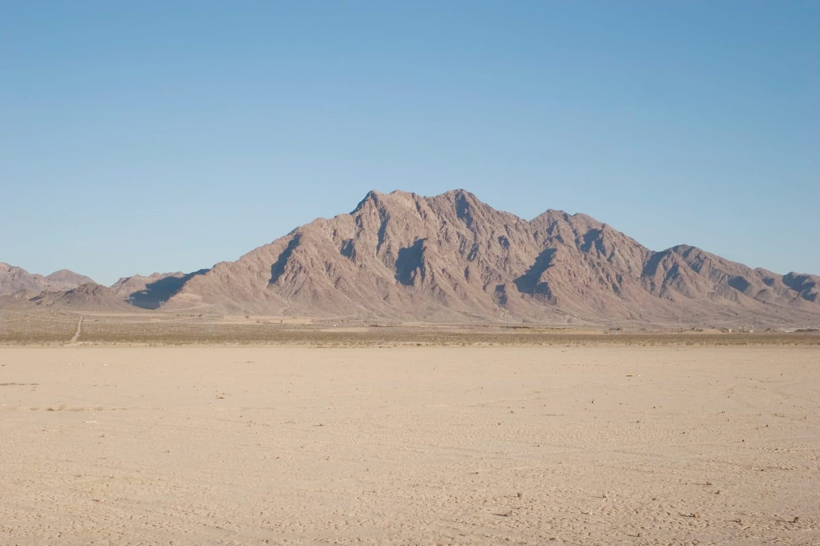 The flat, cracked floor of the dry lake bed outside Las Vegas, NV, with a bare desert mountain rising behind it under an open blue sky